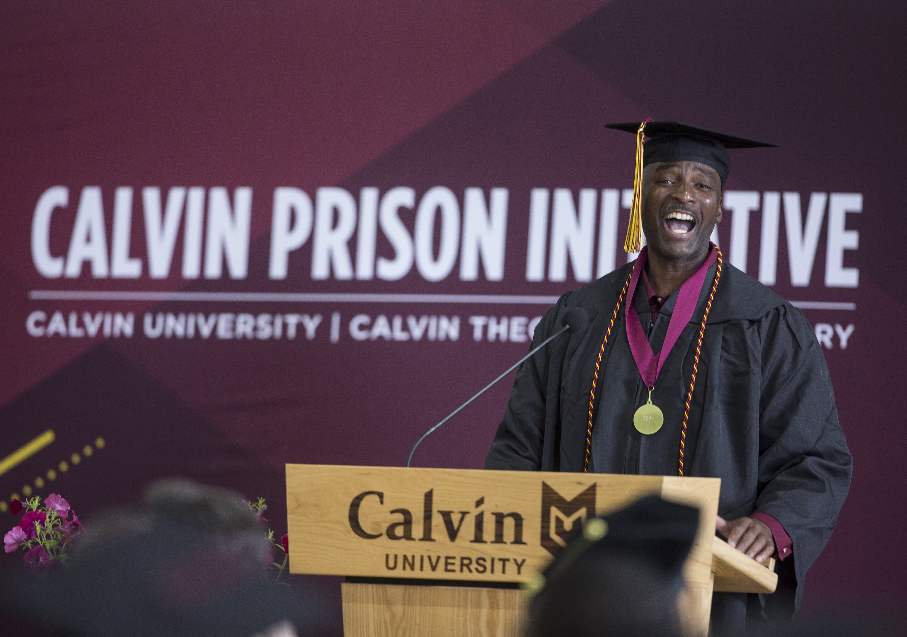 A Calvin Prison Initiative graduate stands at a podium in his graduation cap and gown.