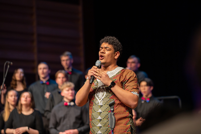 A student performs a solo while the rest of the vocal ensemble stands behind.