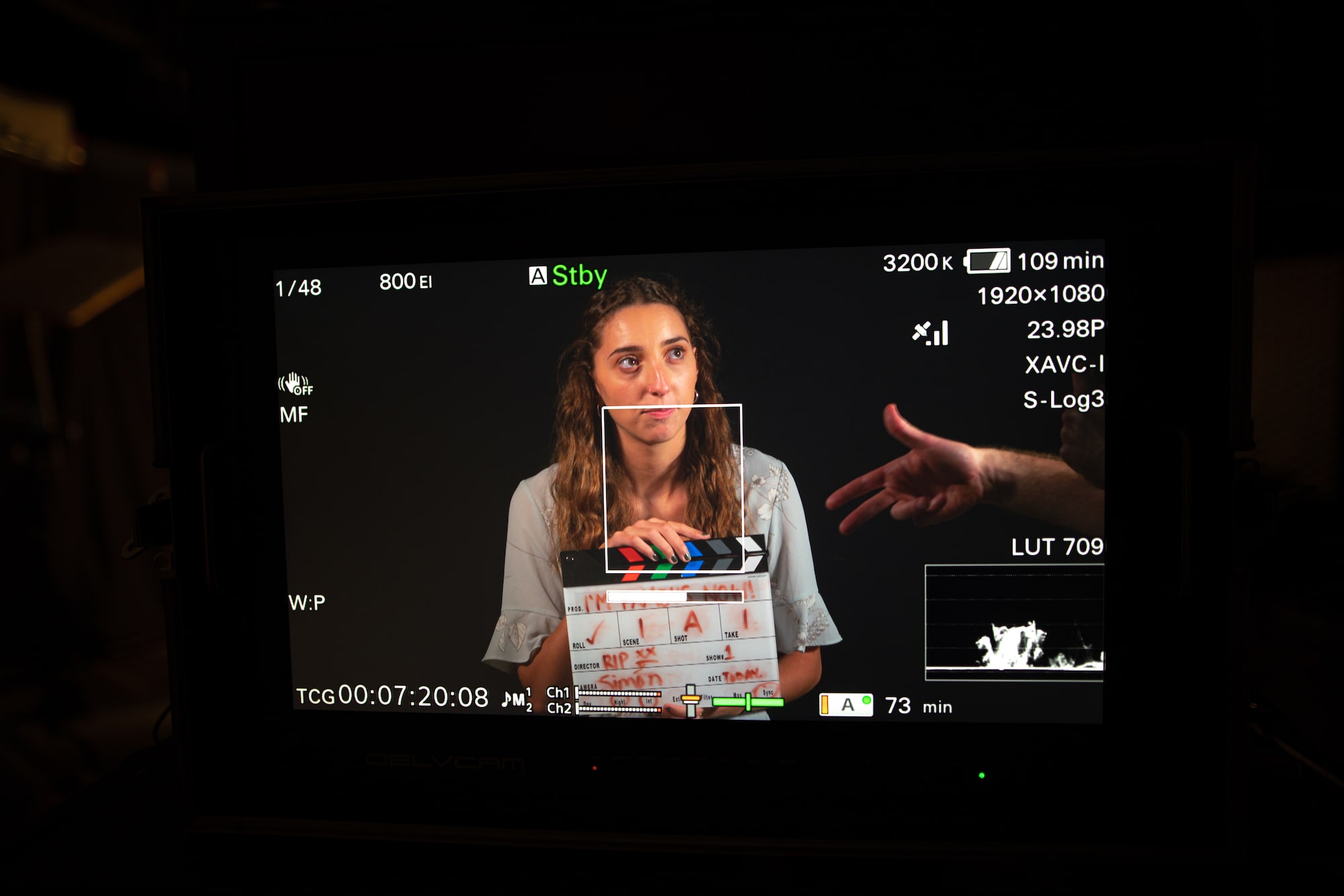 The screen of a digital camera focuses on a student holding a clapboard.