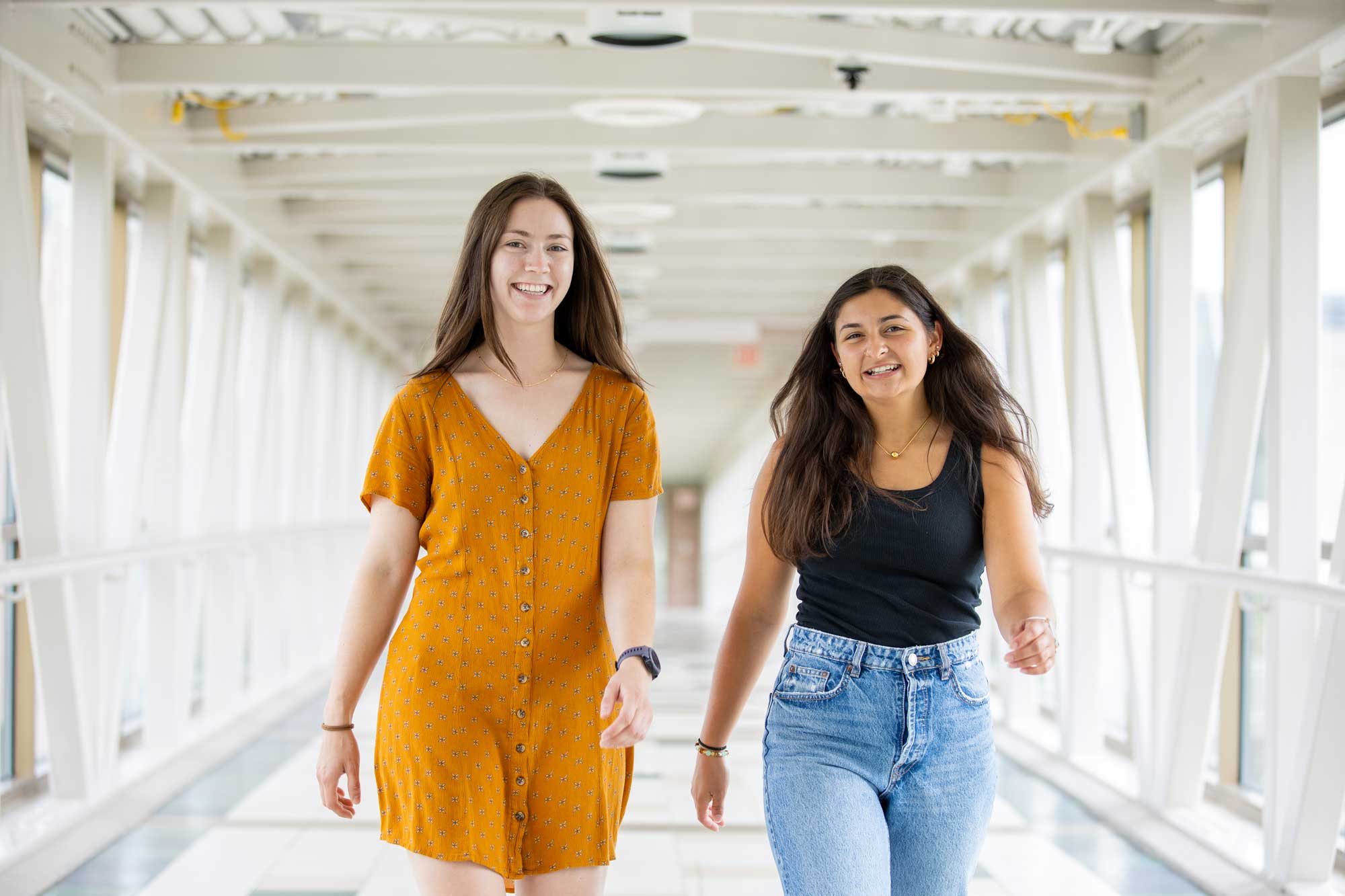 Two Calvin students walk across the overpass, smiling and walking toward the camera.