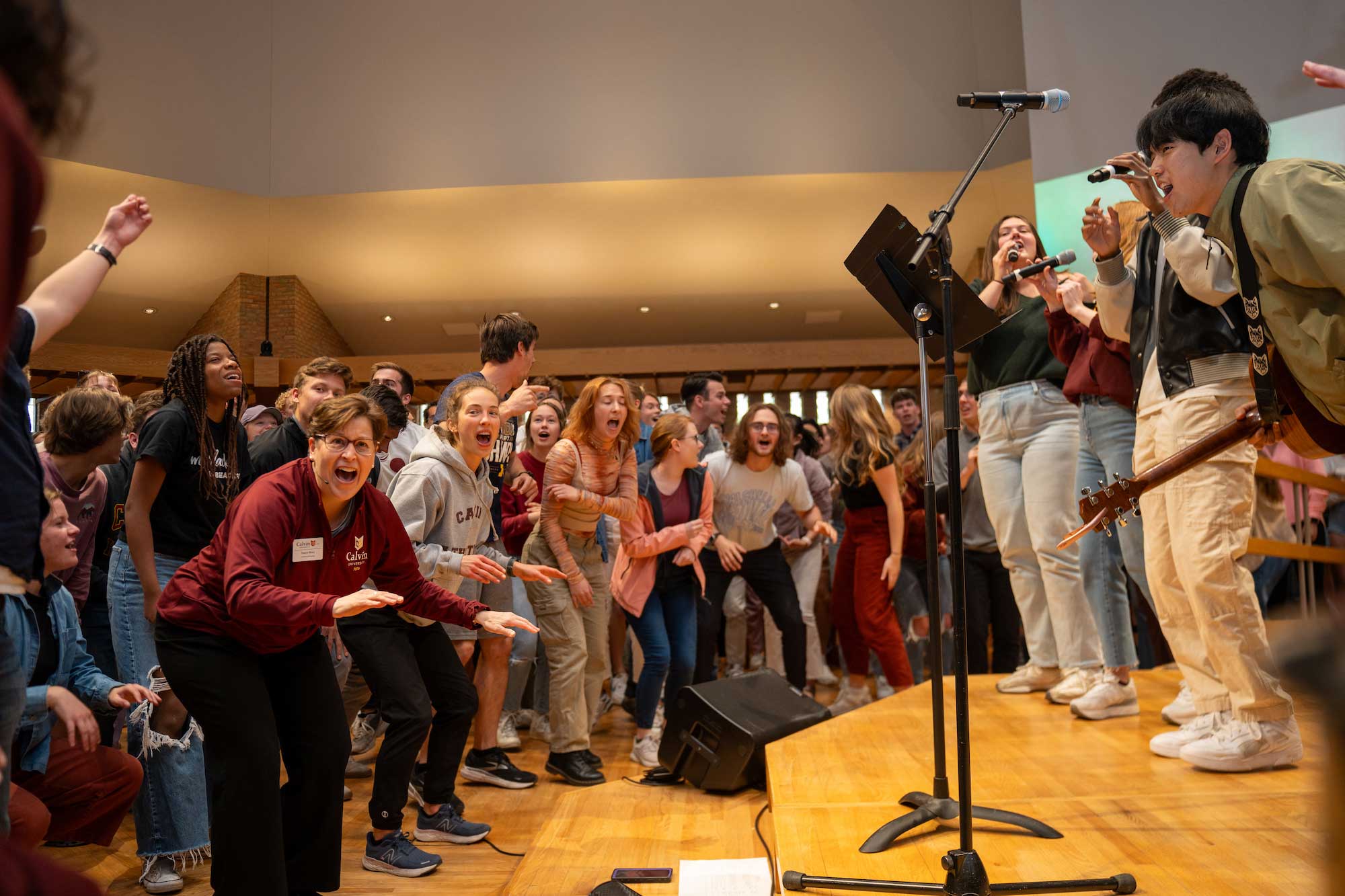 The Calvin student worship team leads at the front of chapel, while students and staff sing and cheer energetically.