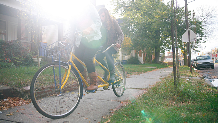a person riding a bike on the sidewalk, sunshine coming in through the background