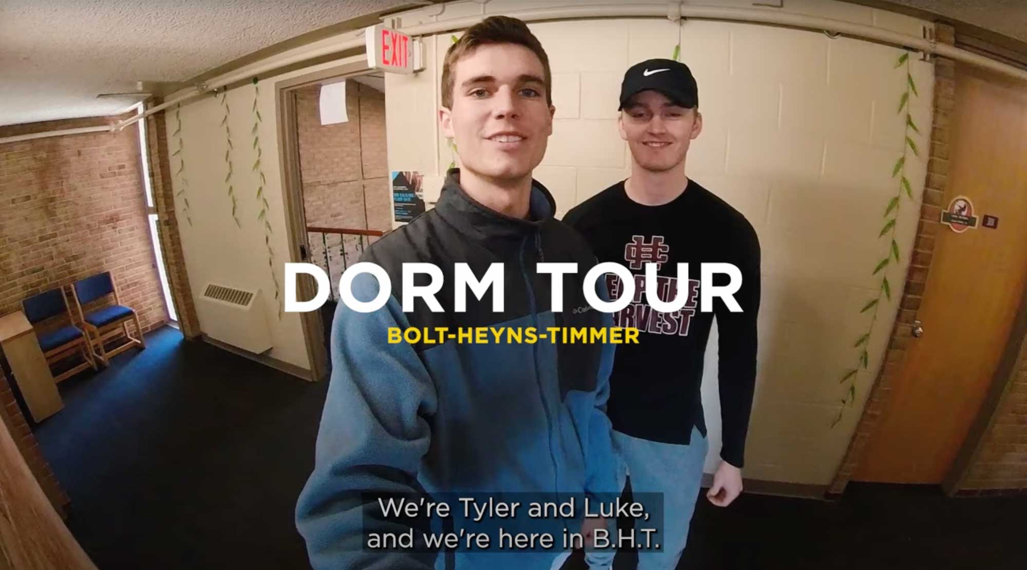 Two male students hold the camera in front of the door to their dorm.