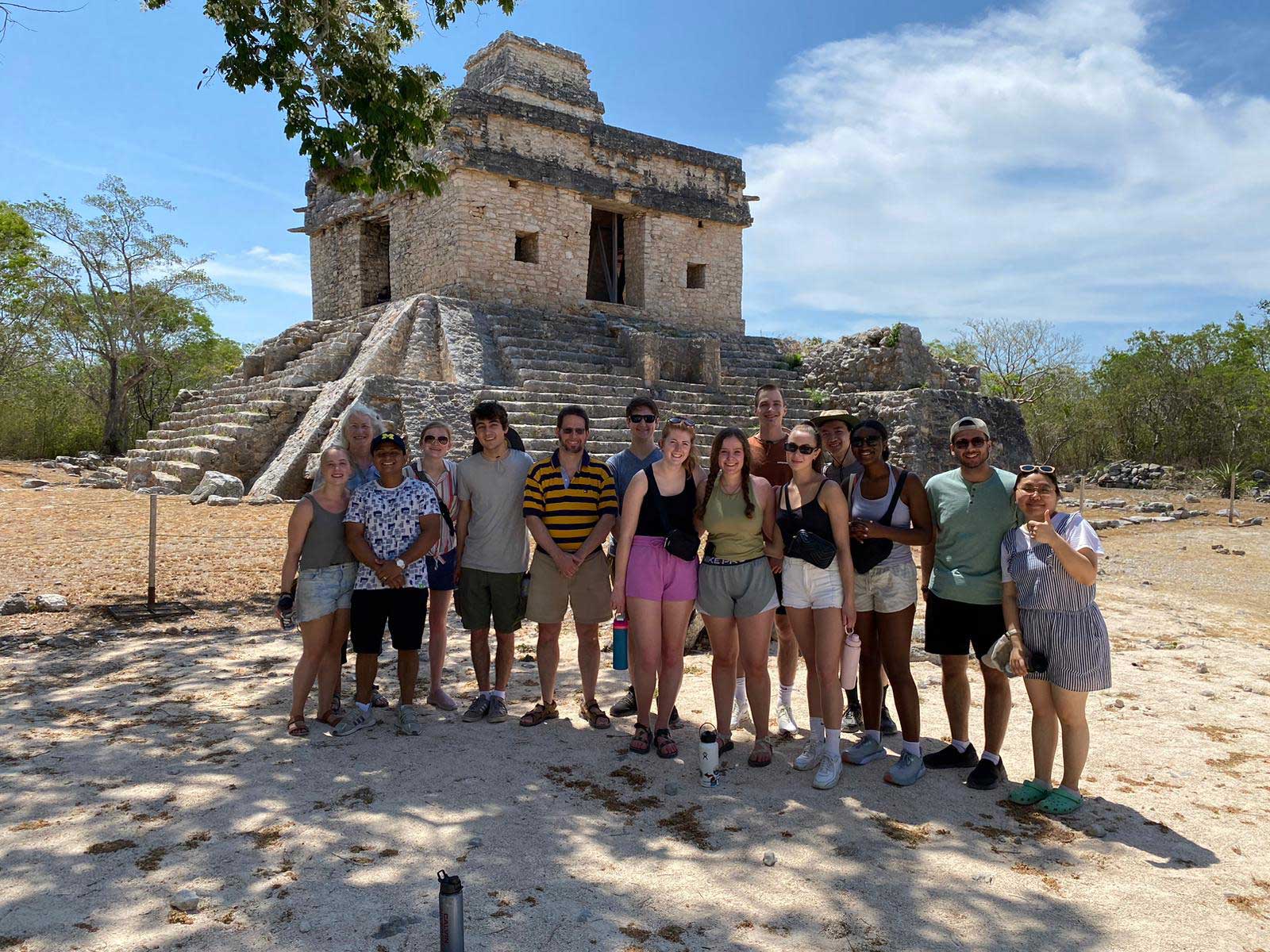 A group of students and professors stands in front of Mayan ruins in Mexico, on a sunny day with blue skies.