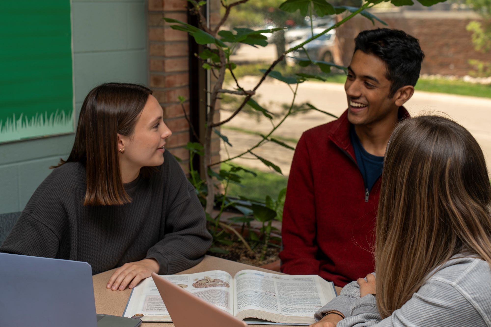 Three students talking near an open textbook