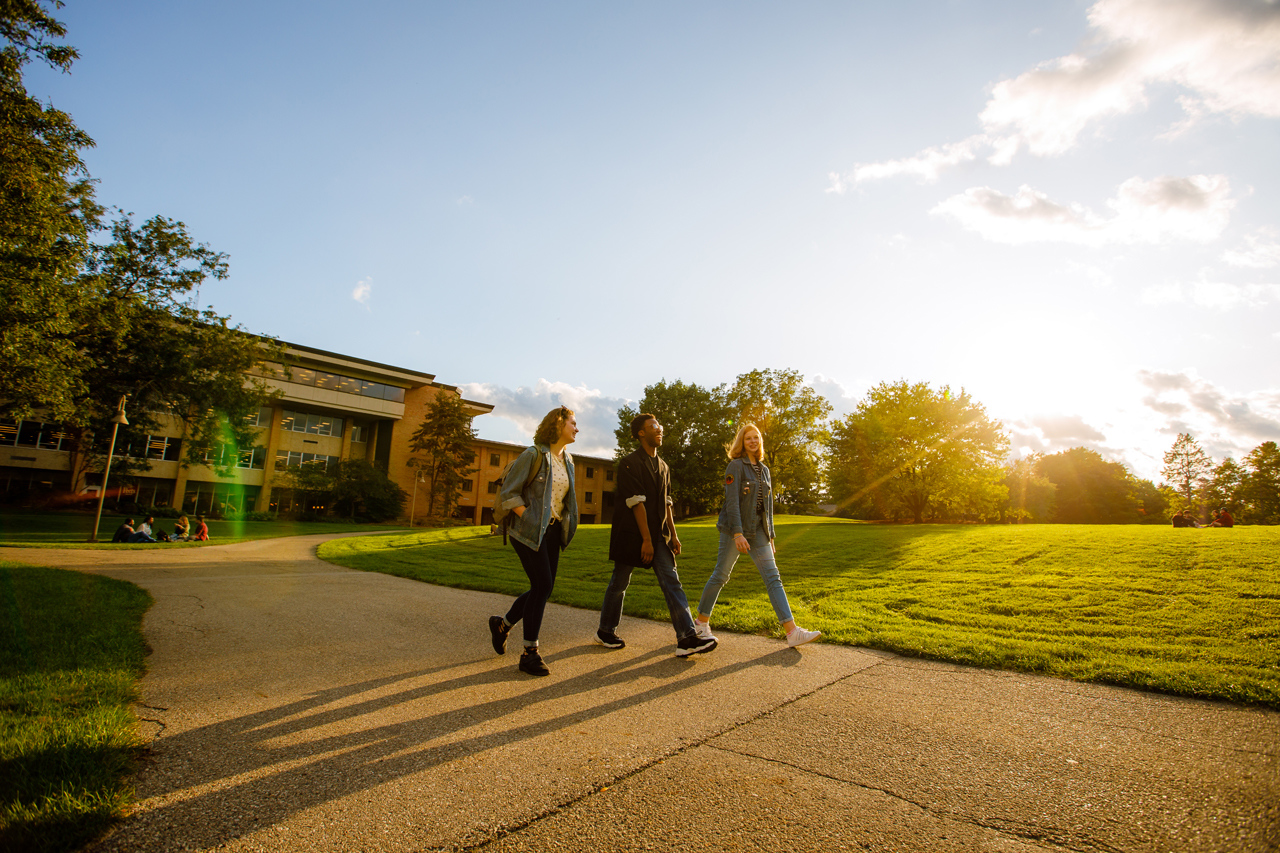 Three students walk near commons lawn at Calvin University as the sun sets.