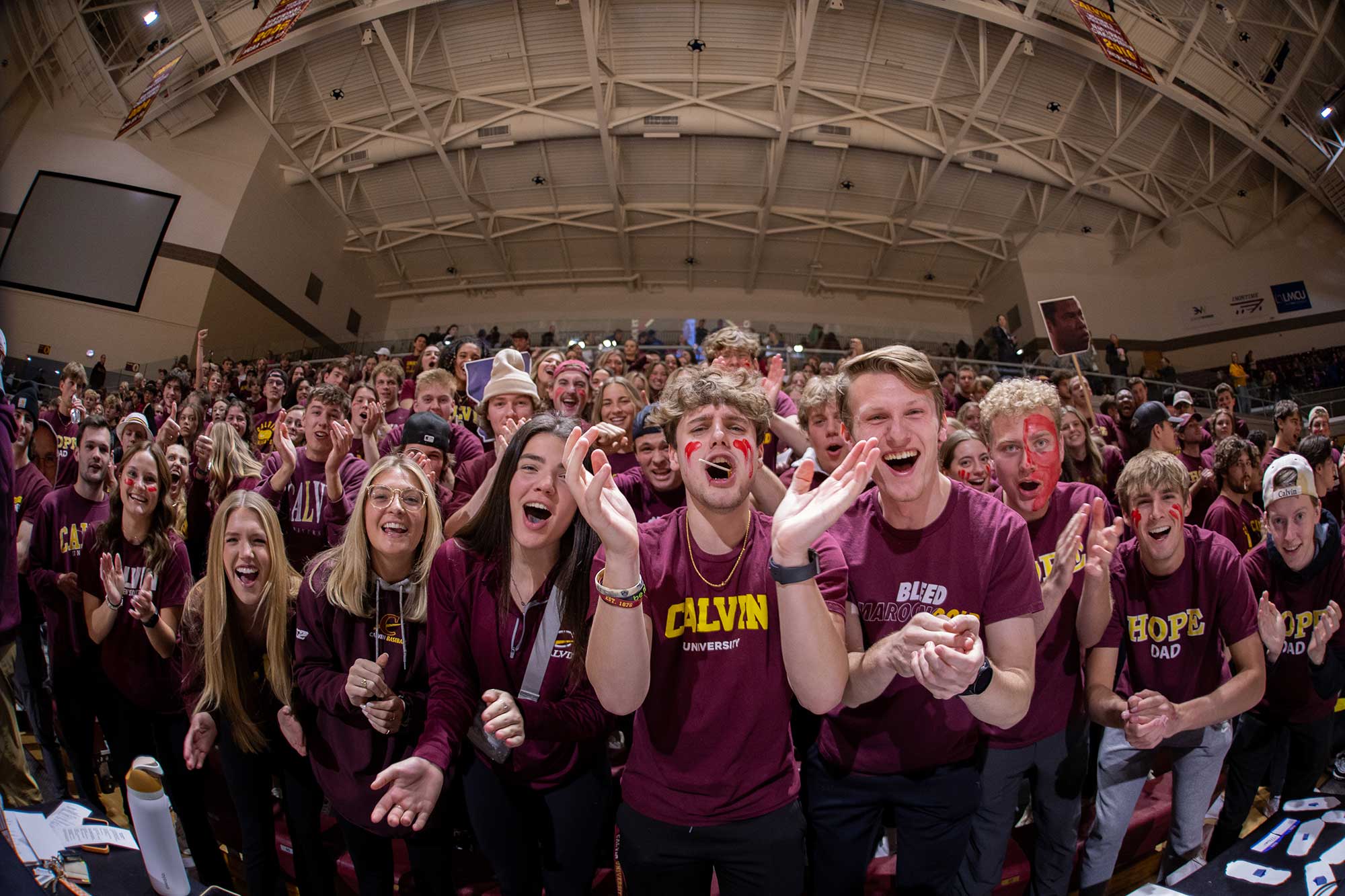 The student section wearing maroon shirts and red face paint cheers on the men's basketball team at Calvin.