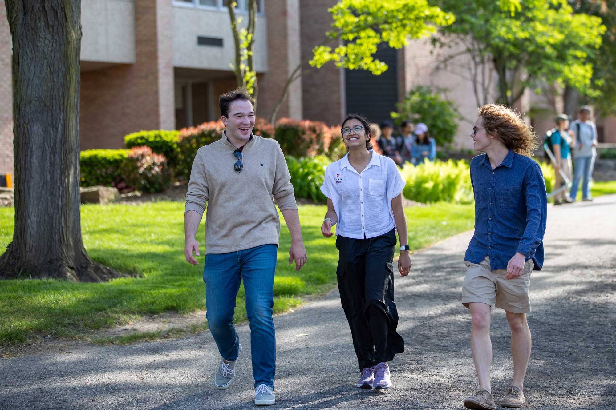 Three Calvin students walk on the path outside the library.