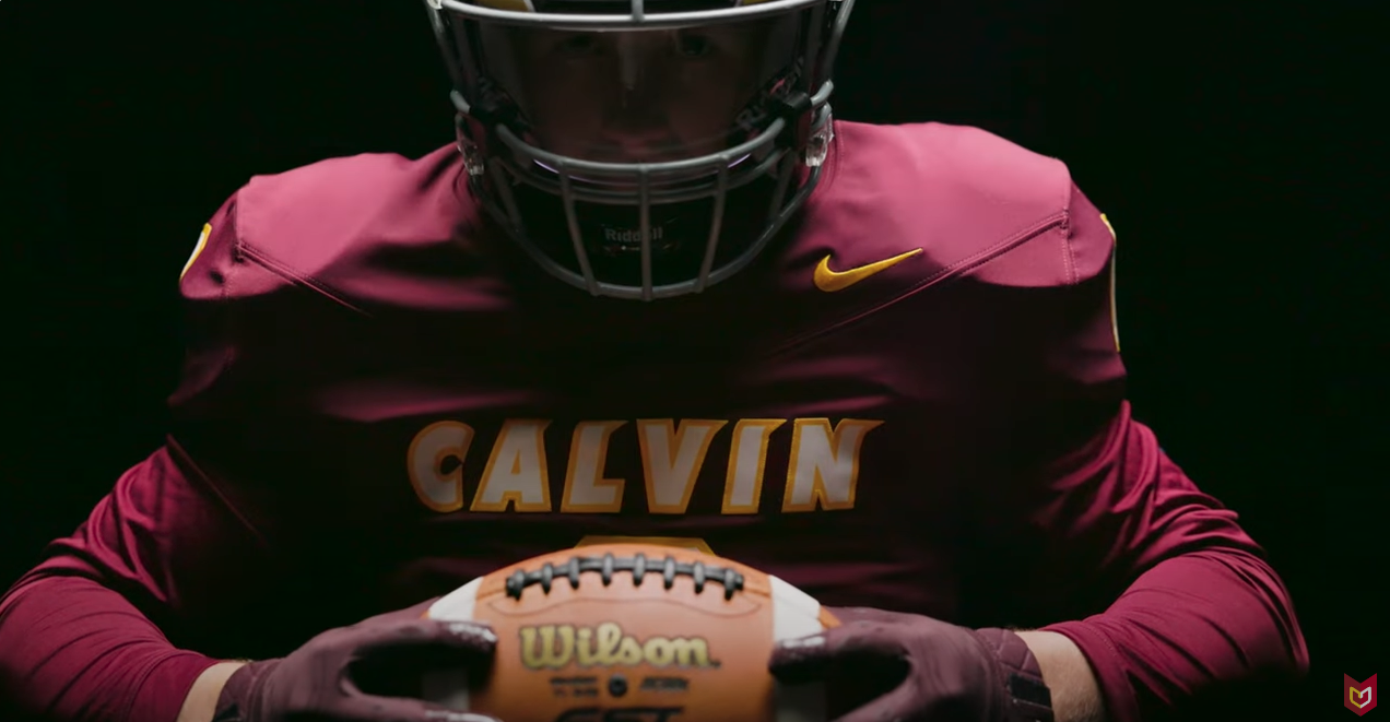 A calvin football player in uniform holds a football, against a black background with dramatic lighting.