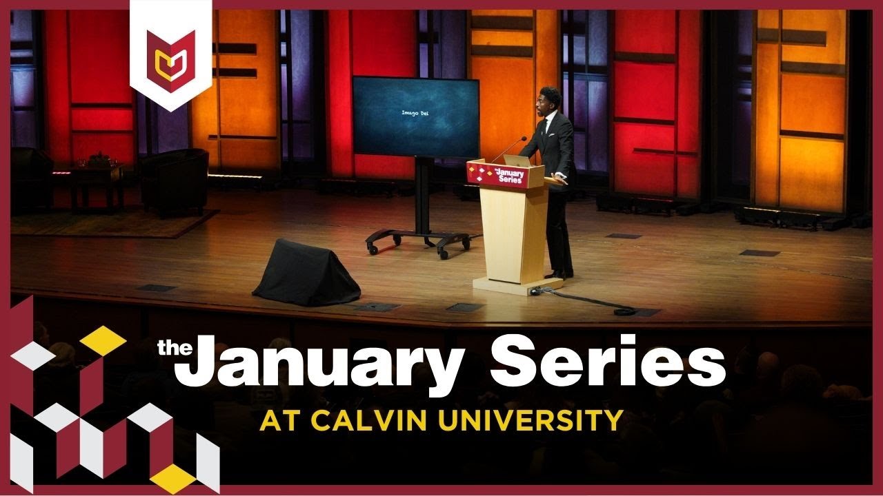 A January Series speaker stands on the stage with red and yellow lights lit behind.