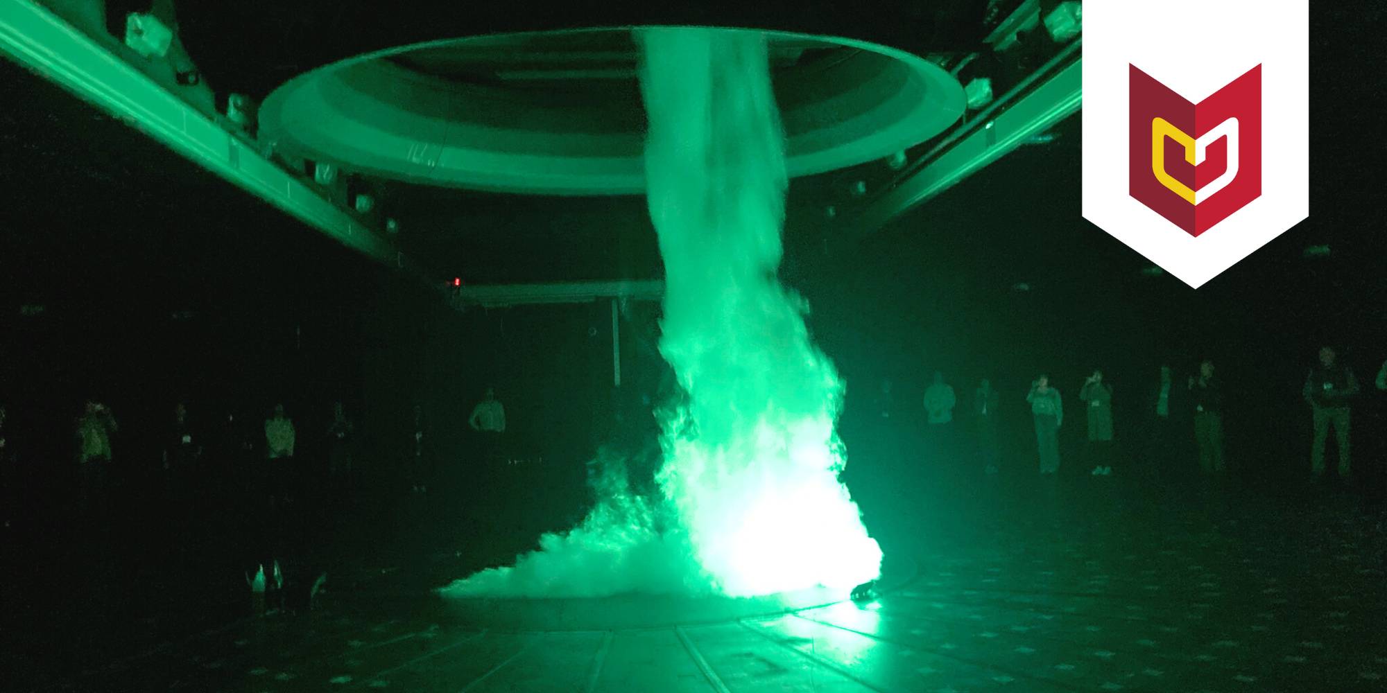 A Tornado Simulator in the dark with a green light shining through the smoke.