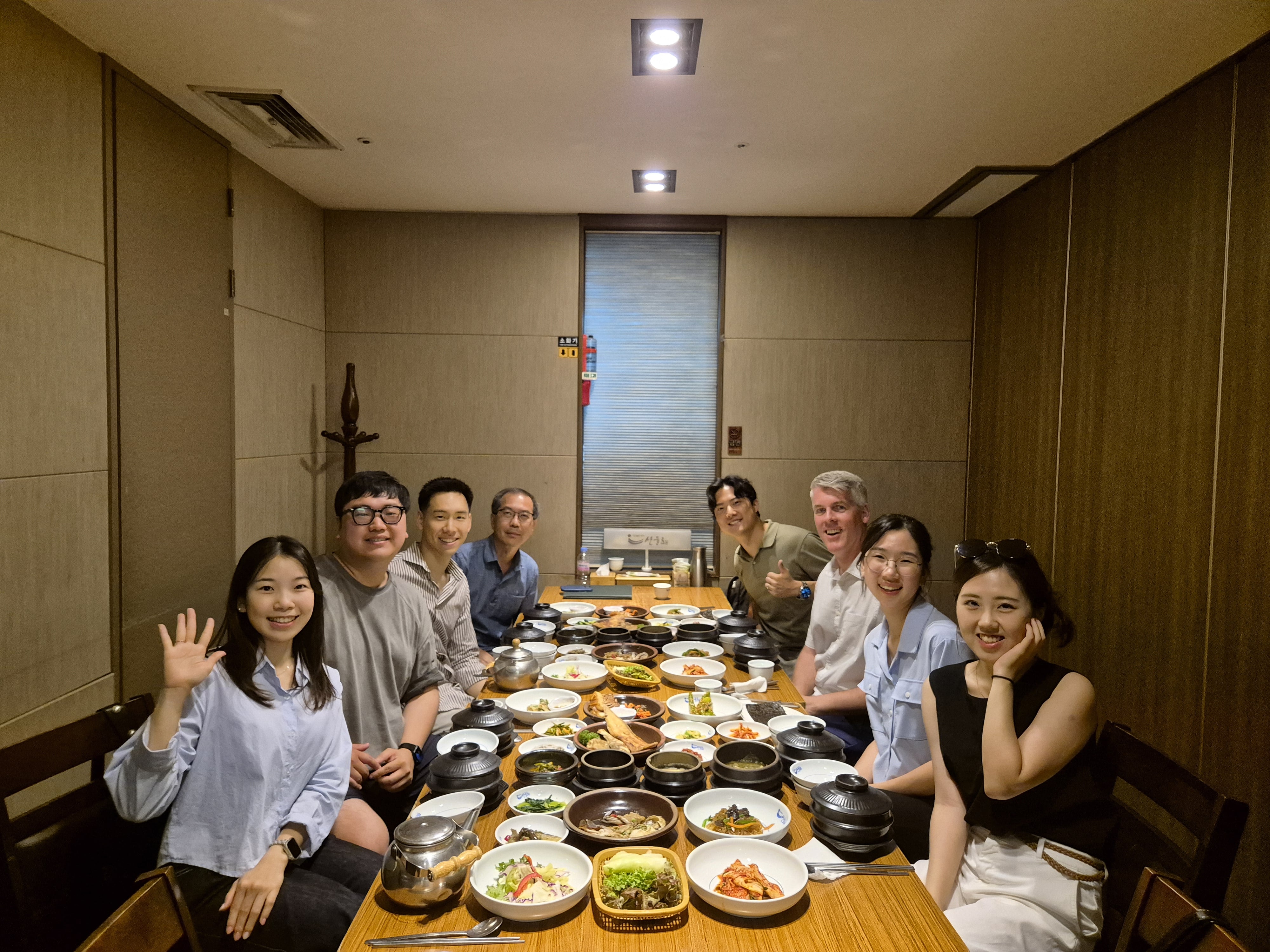 Seven Calvin alumni gathered around a dinner table, with one waving at the camera