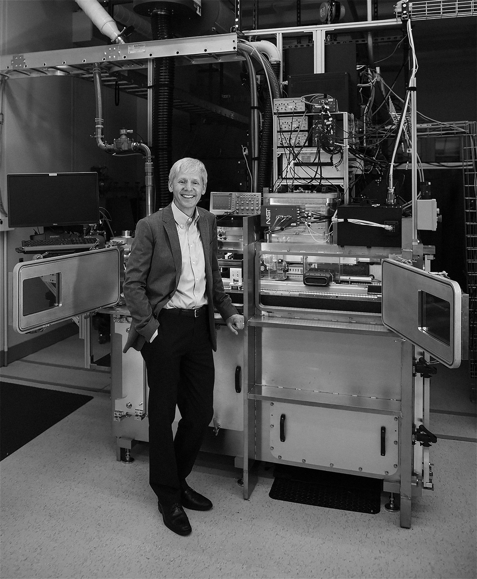 2024 Distinguished Alumni Award winner, Jim Olthoff, stands smiling in front of a scientific machine in his workplace