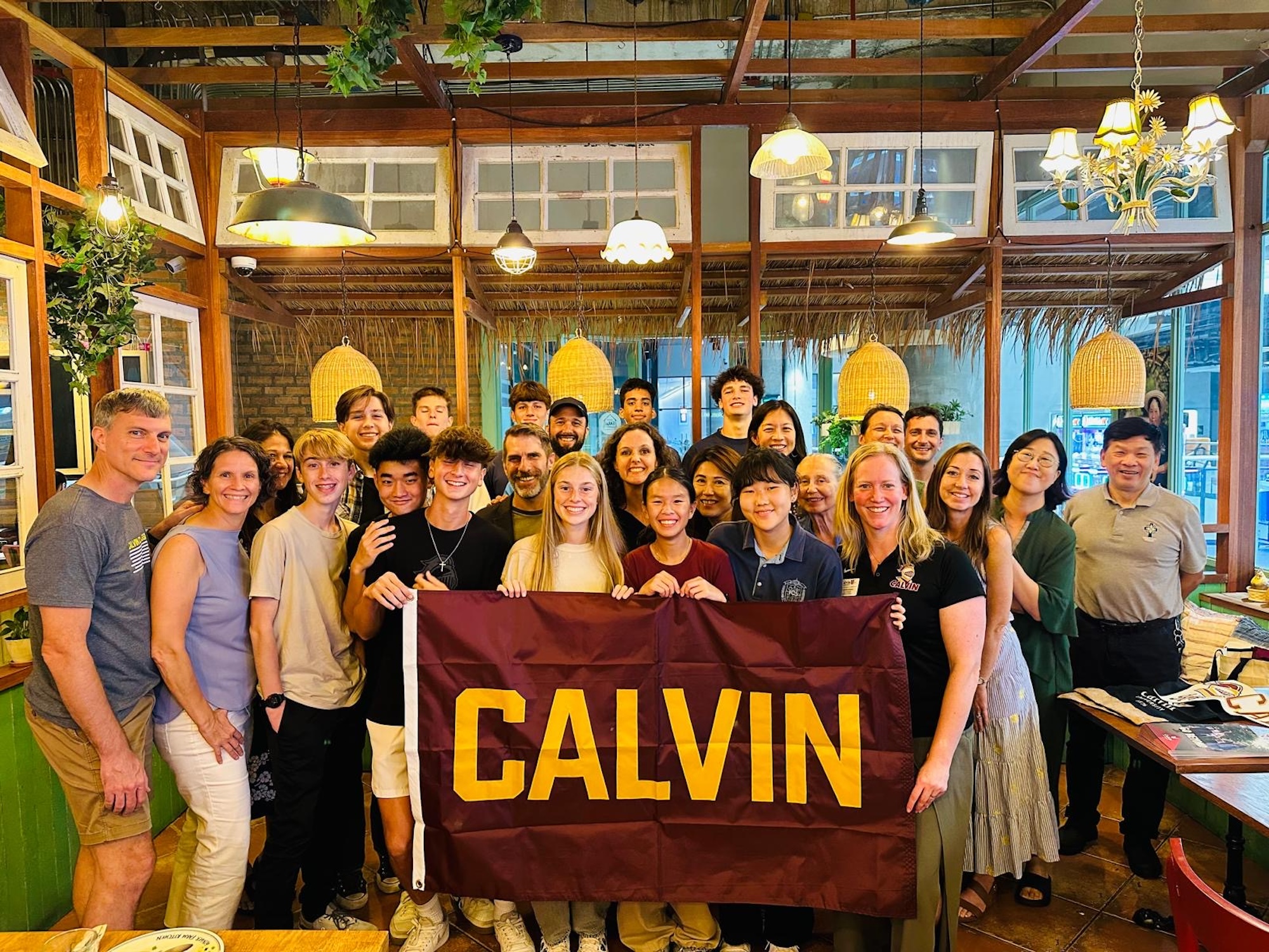 Group of Calvin University alumni and prospective families, holding a maroon and gold flag