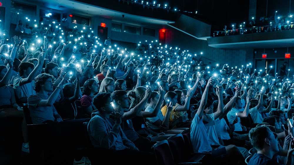 Calvin students in the darkened fine arts center holding up their phones with lights toward the stage