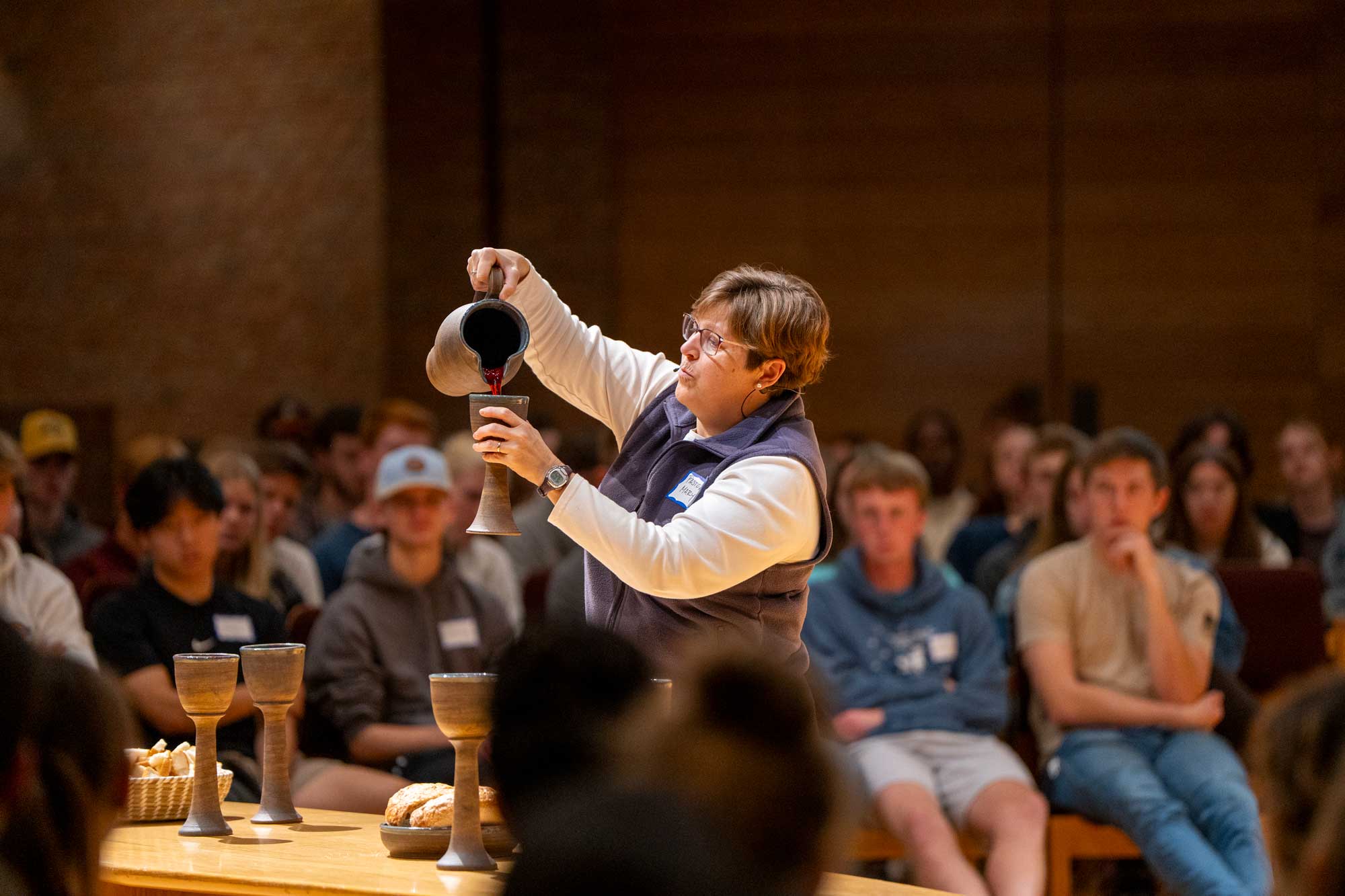 Pastor Mary pours juice into a goblet, introducing the Lord's Supper at a LOFT service at Calvin University.