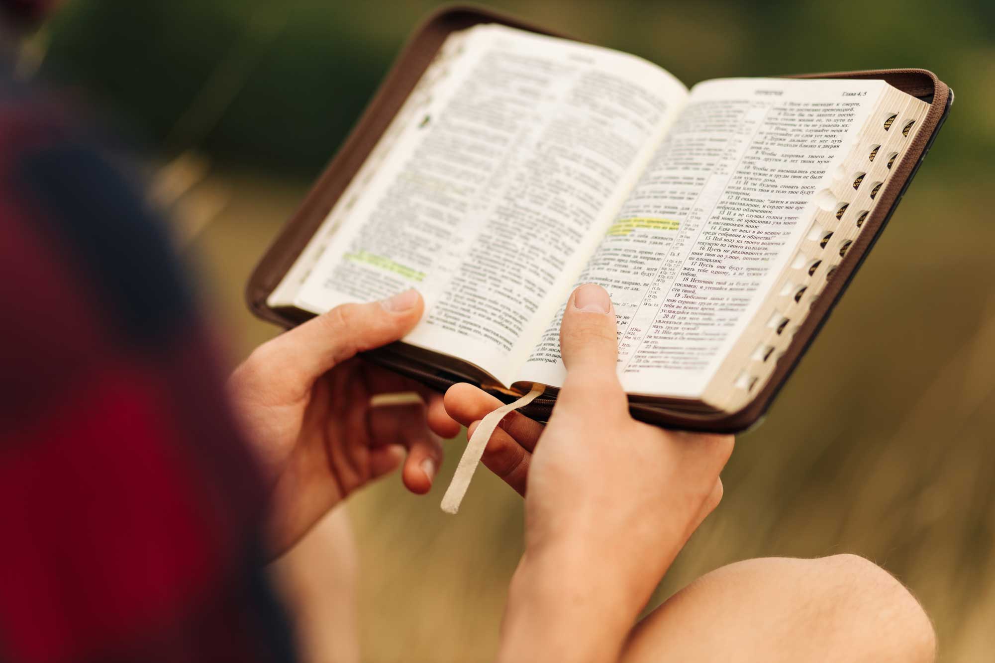 Two hands hold an open bible, with some text highlighted.