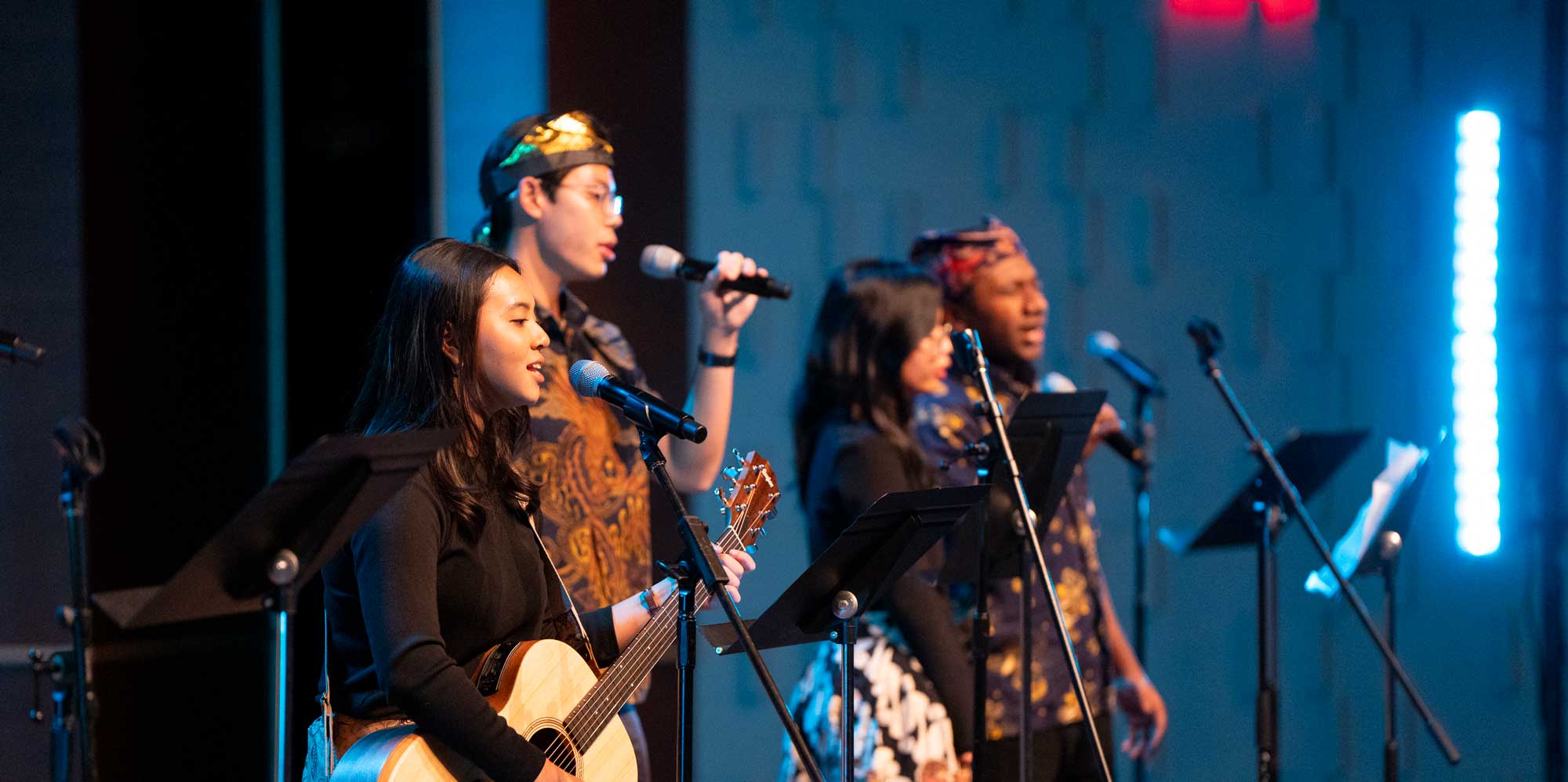 A diverse group of students leads worship with singing and guitar.