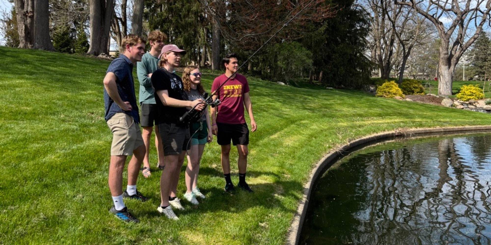 Five engineering students at Calvin University testing out their senior design project, an accessible fishing pole.