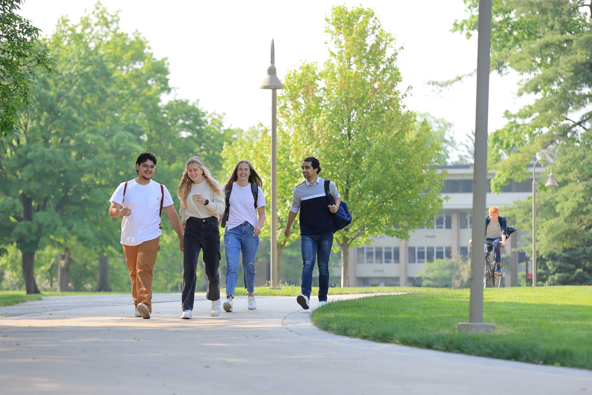 Four students wearing backpacks walk together on the path through Calvin University's campus.