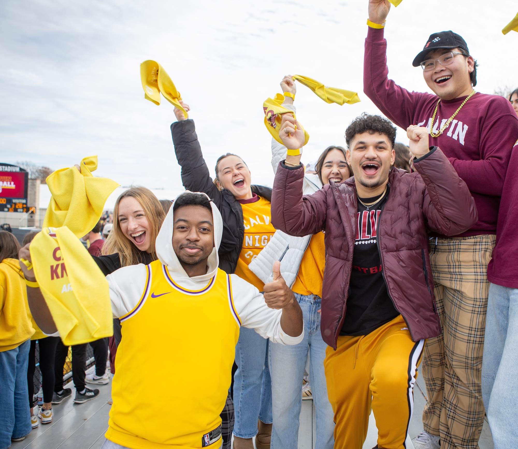 Fans wave towels, cheering in the stands for the Calvin-Hope football game, dressed in maroon and gold