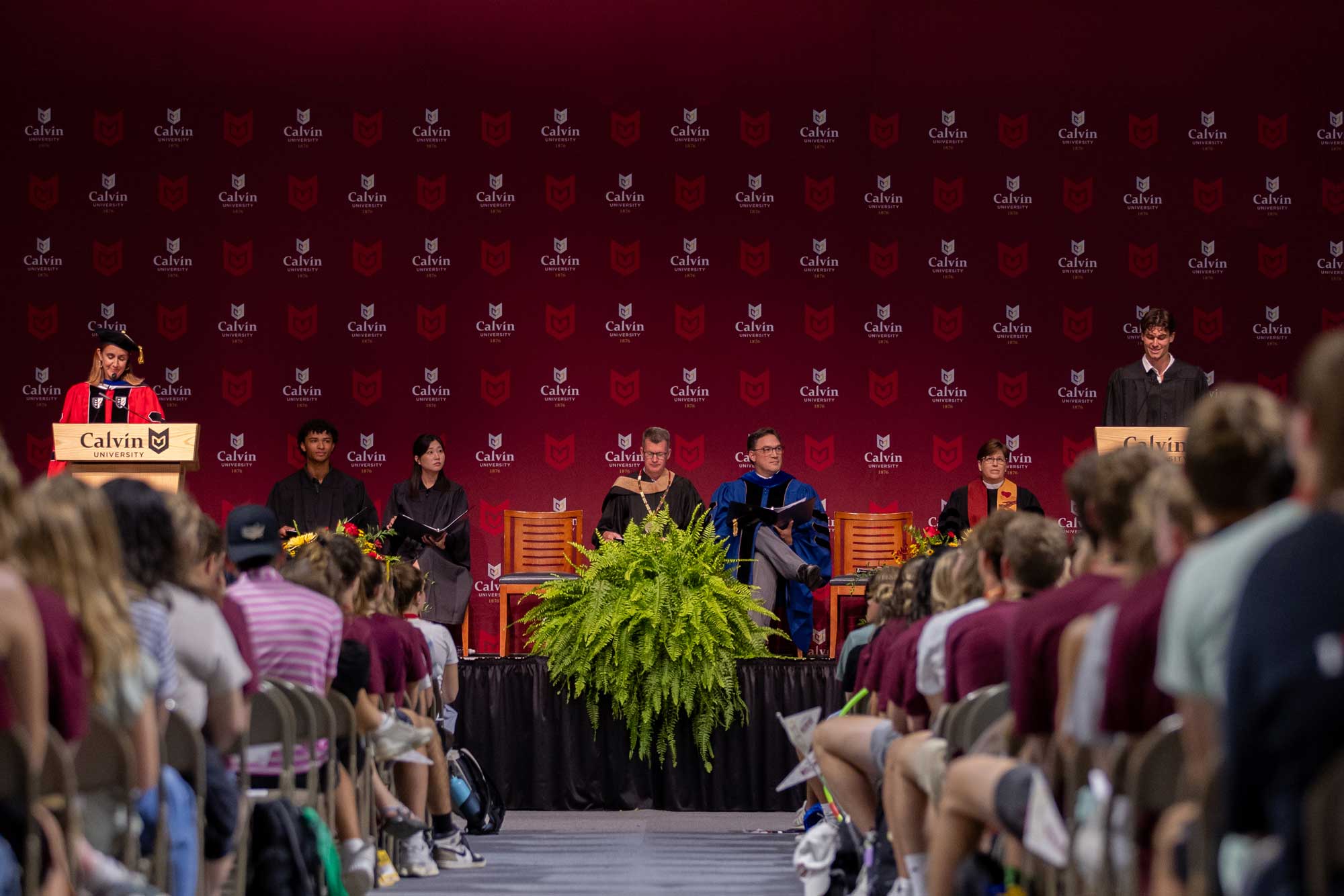Leaders of Calvin University sit on the stage at opening convocation while the student body president gives and address, and incoming students fill the seats.