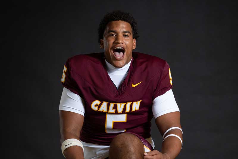 KJ Harp, in a maroon Calvin footbal jersey, poses in celebration against a black backdrop.