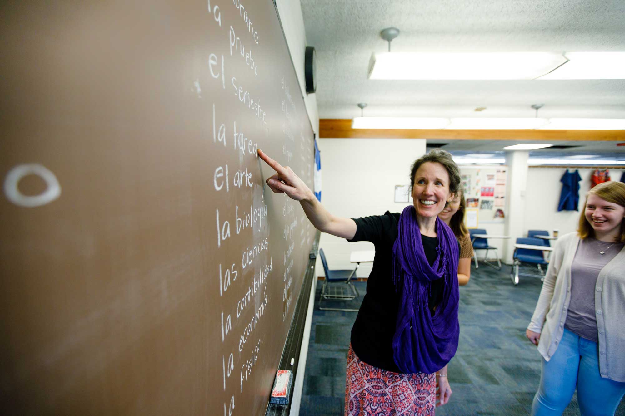 A Spanish professor points to the chalkboard with vocab words while students look on.