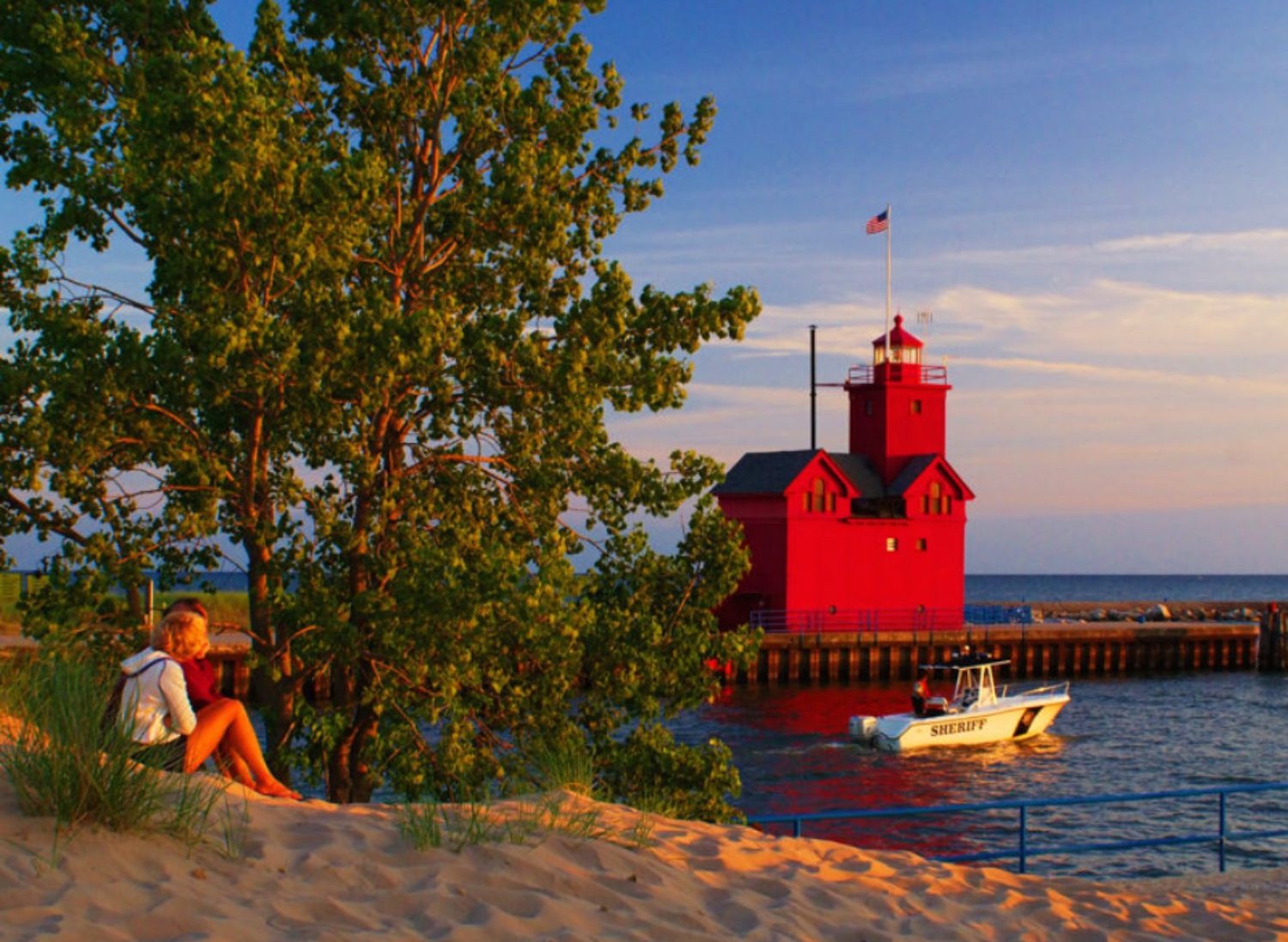 Holland State Beach with red lighhouse water sand and people watching the sunset