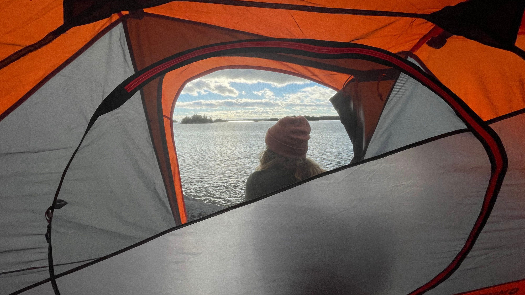 Looking through the door of a tent, with a view of a lake and a student taking it all in.
