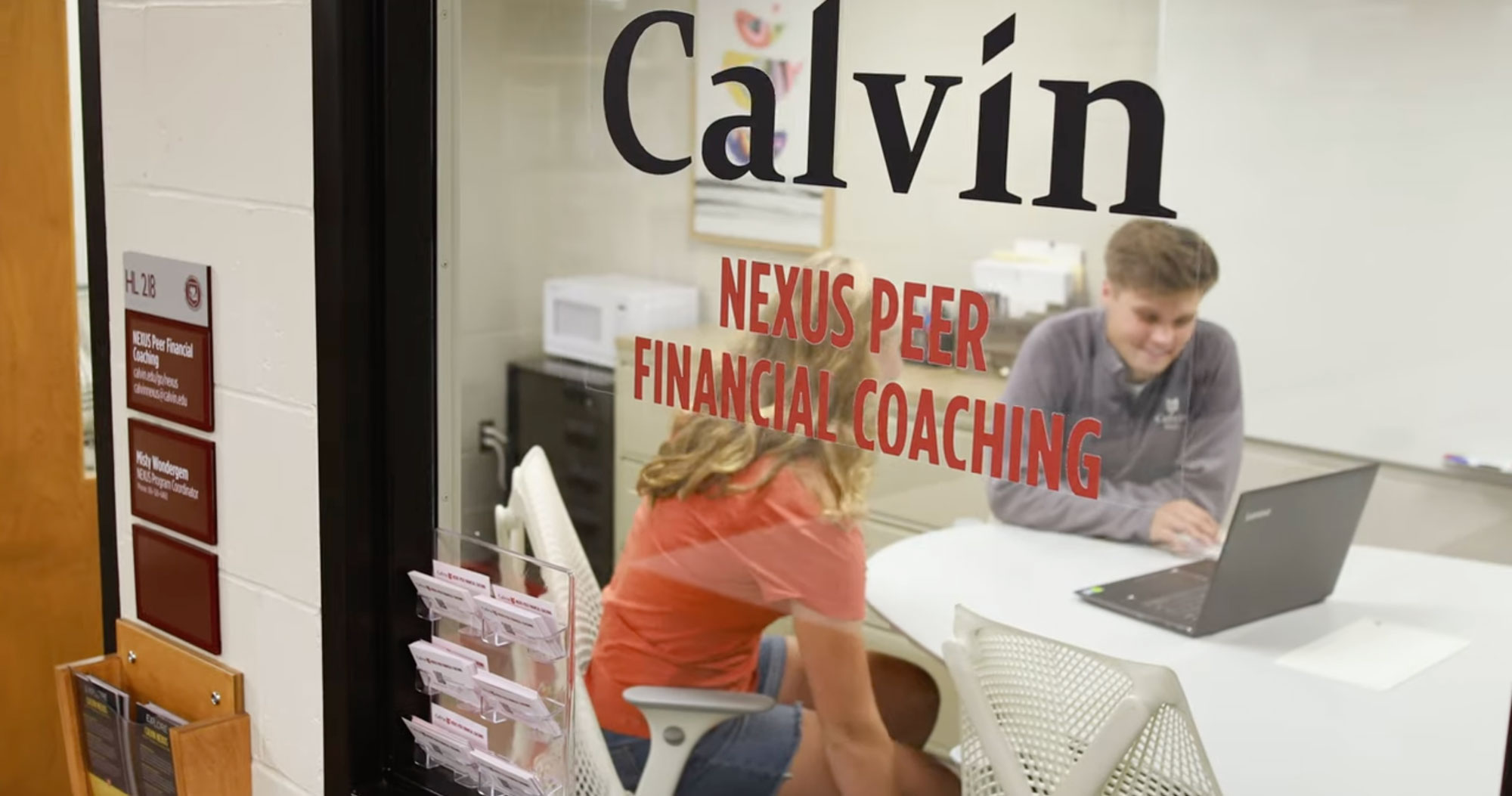 Two students meet in a room with a glass door, with the Nexus name on the wall.