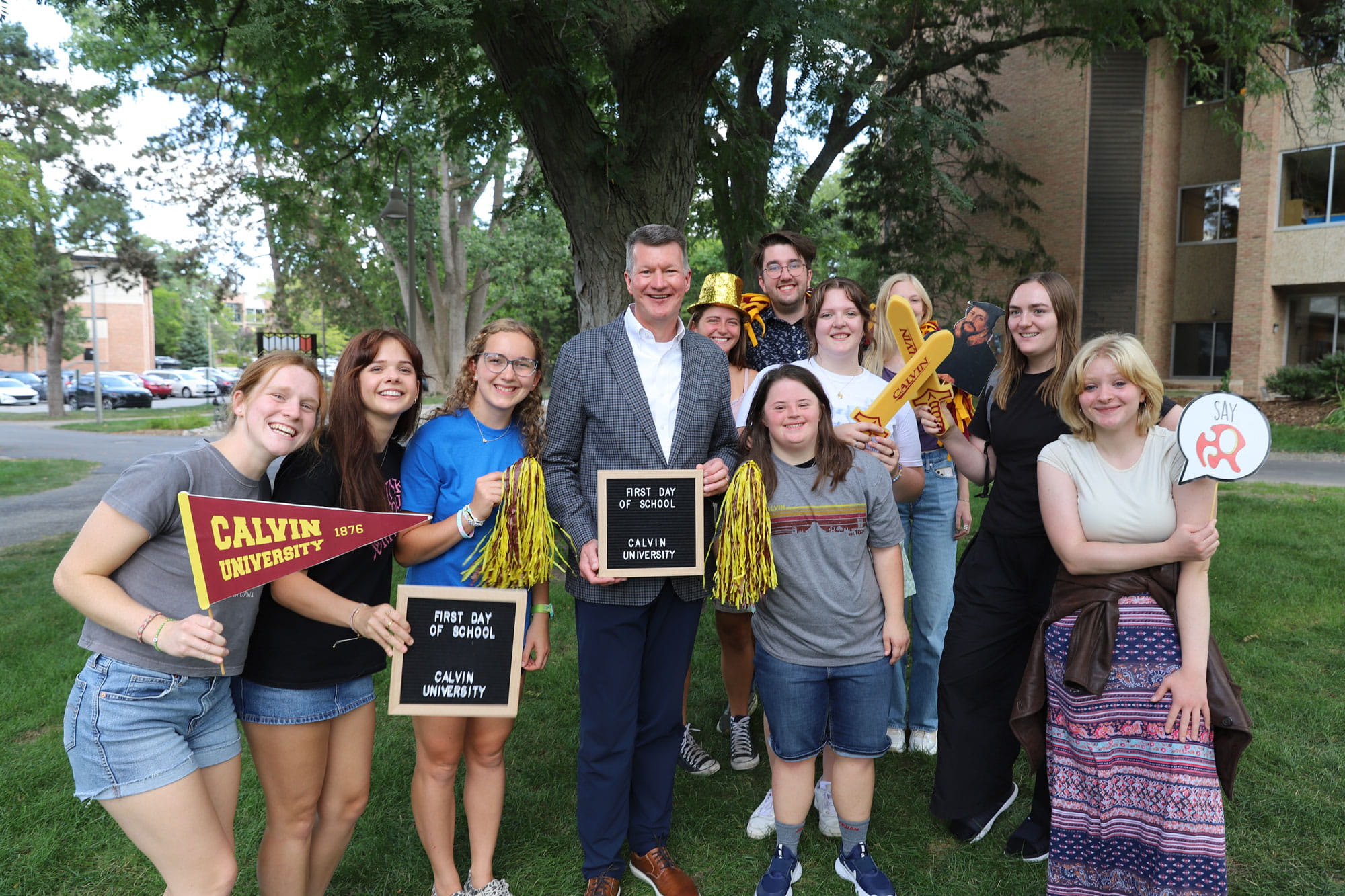 A group of Calvin students gathers with President Elzinga, holding signs for the first-day celebration, Calvin penents, and other photo props.