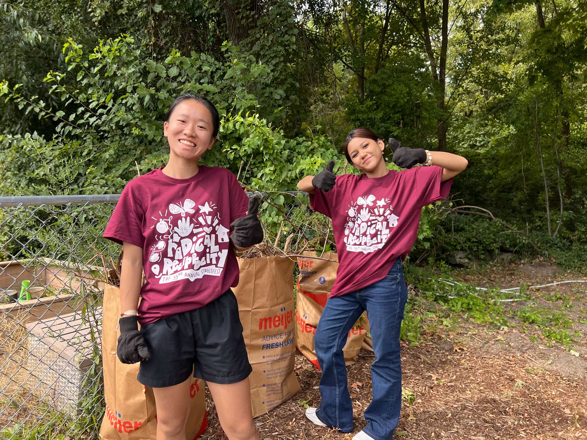 Two new Calvin students in maroon streetfest shirts give thumbs up while doing landscaping work.
