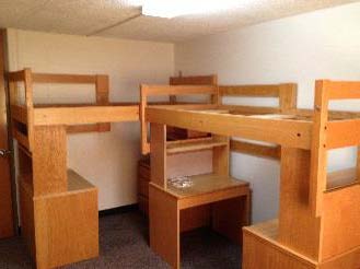 Two beds lofted on top of desk, dresser, and shelf stacks, positioned in the corner of the room.