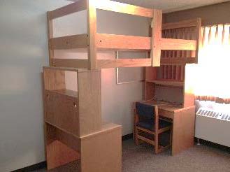 A bed stacked on top of a desk with shelf under one end, and a dresser and bookcase on the other end.
