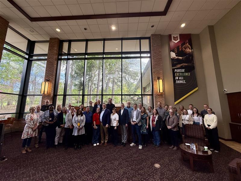 A large group of Calvin faculty, staff, and community gathers with Noah Toly in the large and bright Spoelhof University Center.