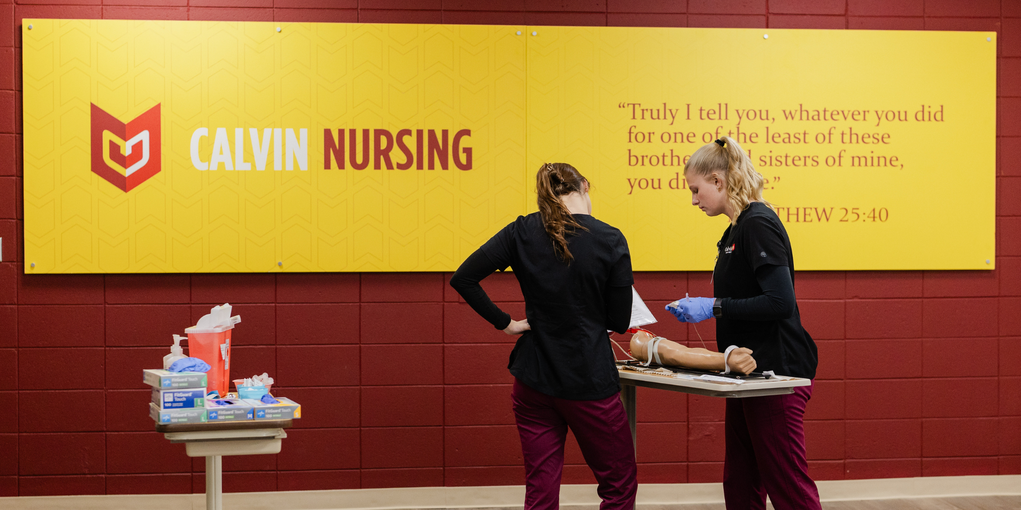 Two Calvin Nursing students practicing placing an IV in he classroom