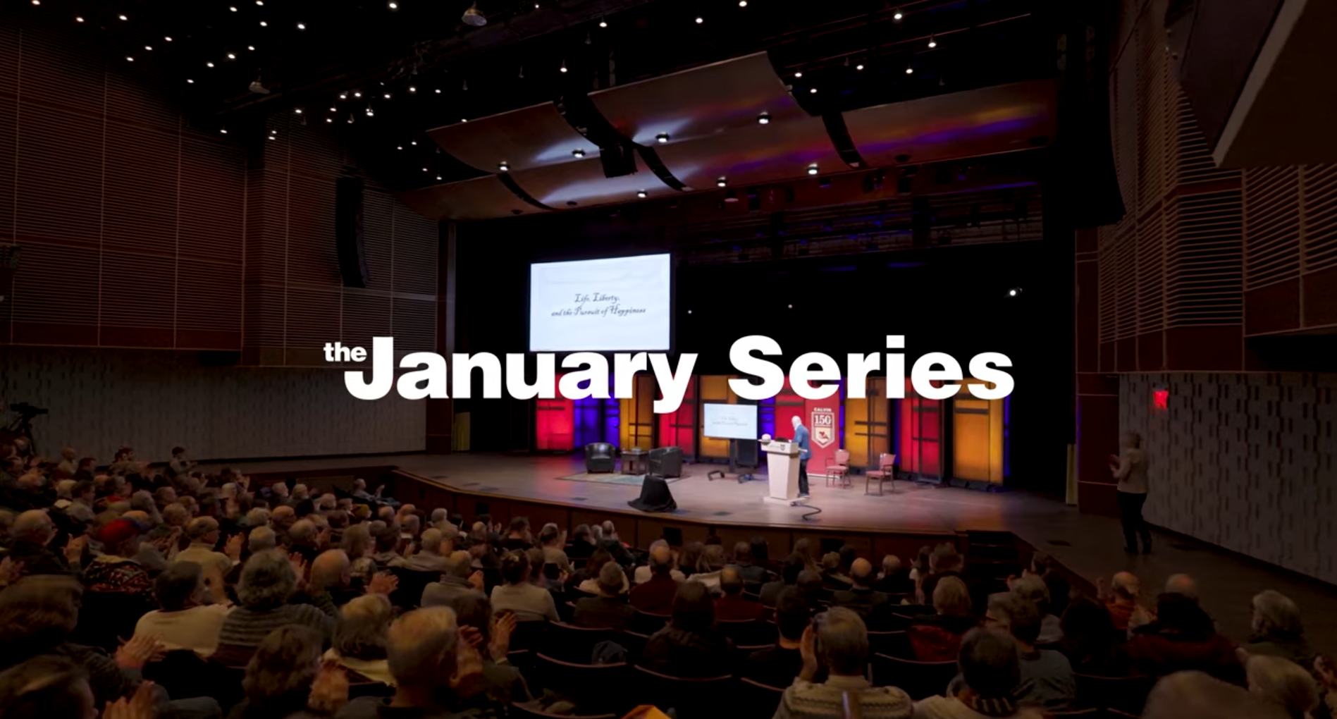 January Series titlecard in front of a large crowded auditorium