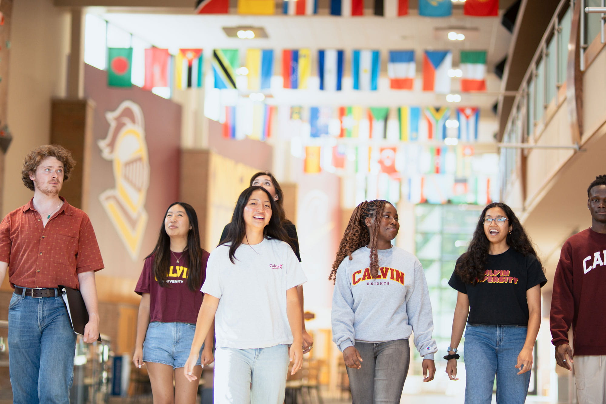 Members of Student Senate wearing Calvin gear walk in a large open lobby with flags of different countries hanging above.