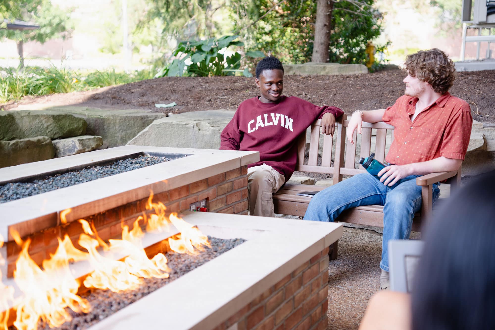 Two students sit by a long brick fire pit on Calvin's campus.
