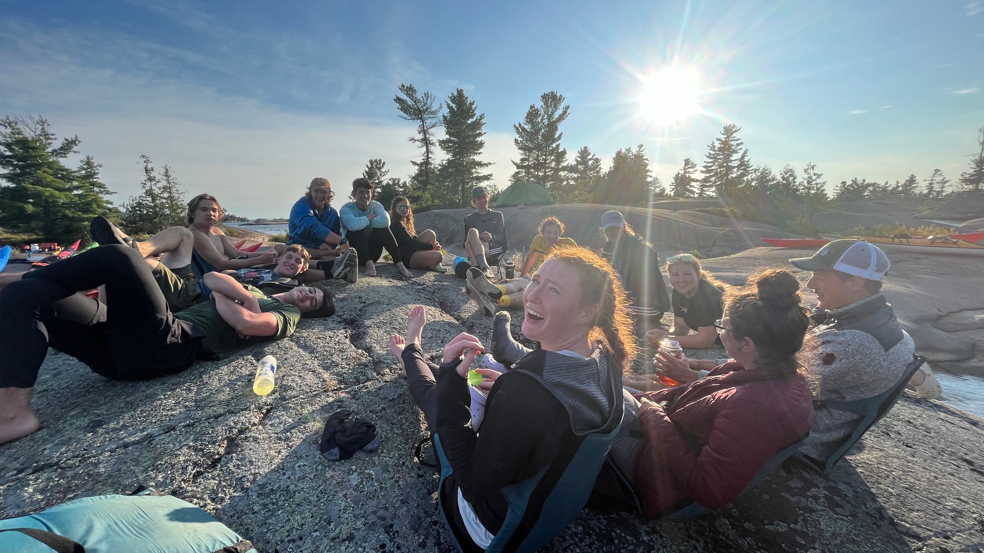 Students sitting on flat rock near a forest with the sun shining