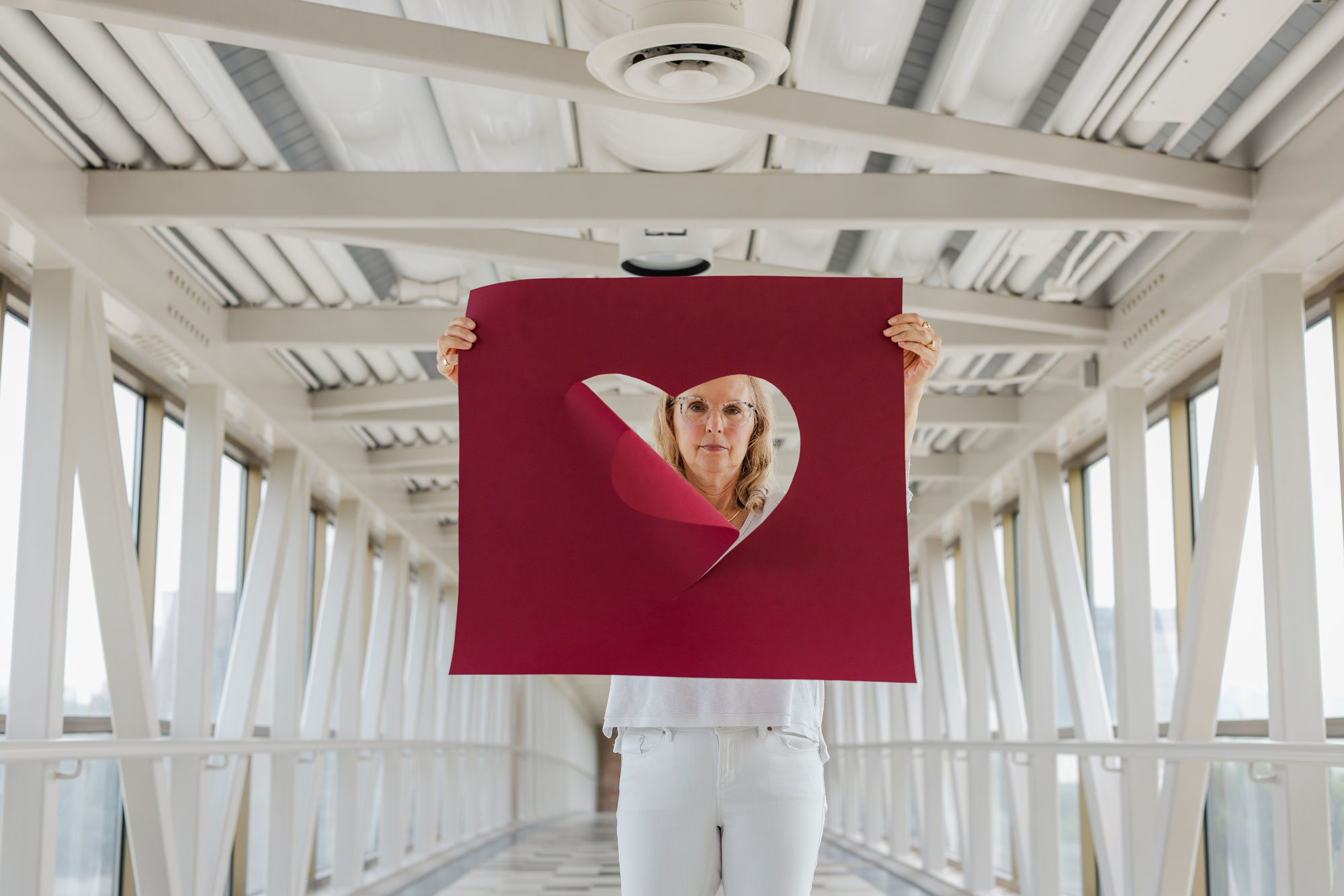 Julie Yonker, a Calvin professor, hold a large maroon poster with a heart cut out of it.
