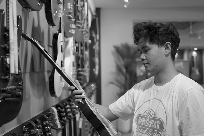 Denny Tawas holds an electric guitar in a music shop.