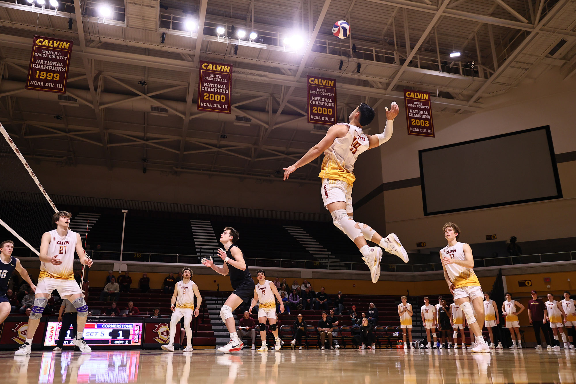 A men's volleyball player leaps in the air for a kill while the teams look on in ready position.