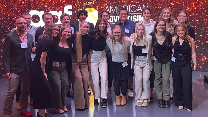 A group of students and their professor standing on stage after they won multiple awards.