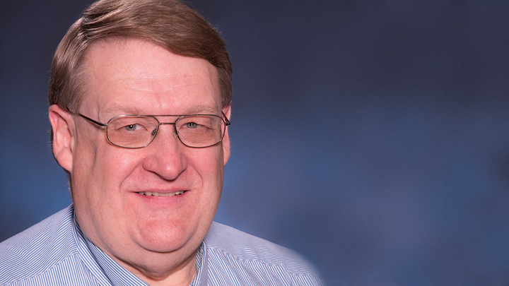 A headshot of a man with glasses against a textured blue backdrop.