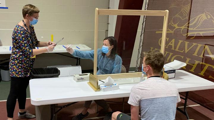 Two women in masks are helping out as a student awaits surveillance testing.