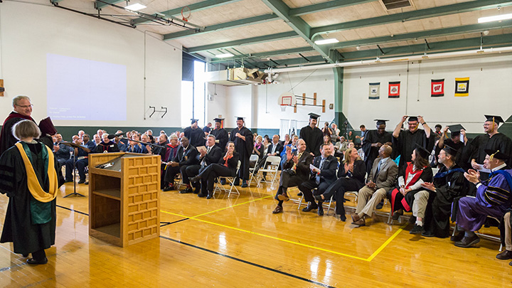 A gymnasium filled with inmates in graduation robes and university faculty in academic regalia