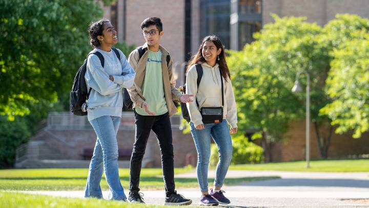 Three international students walking on a spring day on a campus pathway.