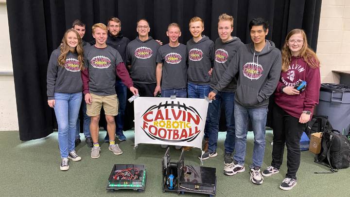 Nine students and their faculty adviser pose with robots and hold a "Calvin Robotic Football" sign.